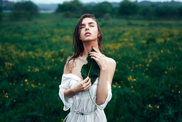 La jeune fille avec une feuille de peine sous la pluie