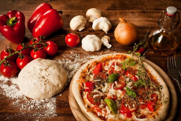 Pizza aux tomates et aux poivrons. Sur la table pâte et légumes