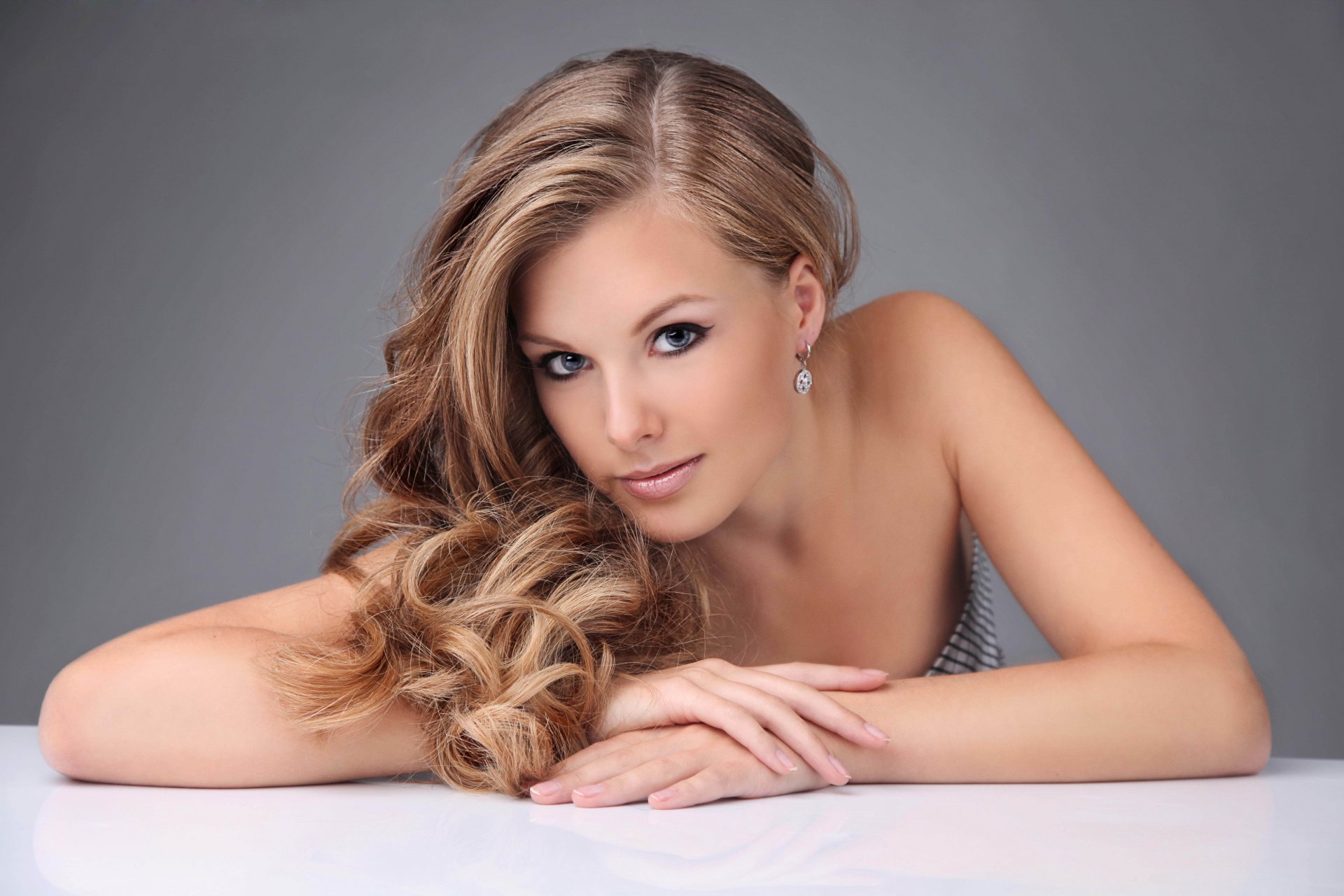 fille blonde visage regard cheveux boucles boucles d oreilles maquillage flèches mains fond gris
